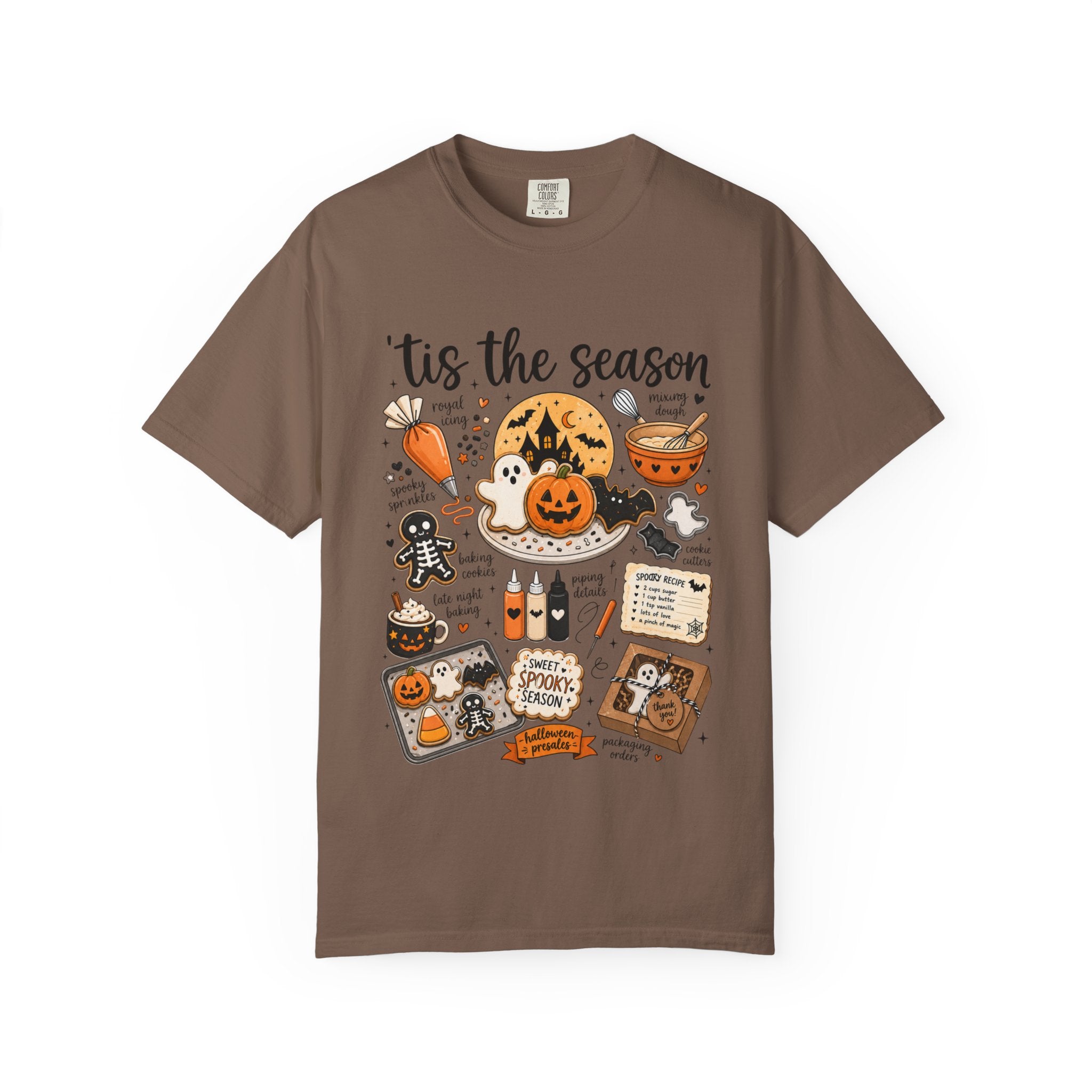 A brown short-sleeve crewneck t-shirt featuring a detailed Halloween-themed graphic print with illustrations of pumpkins, ghosts, a witch, and the text 'tis the season'.