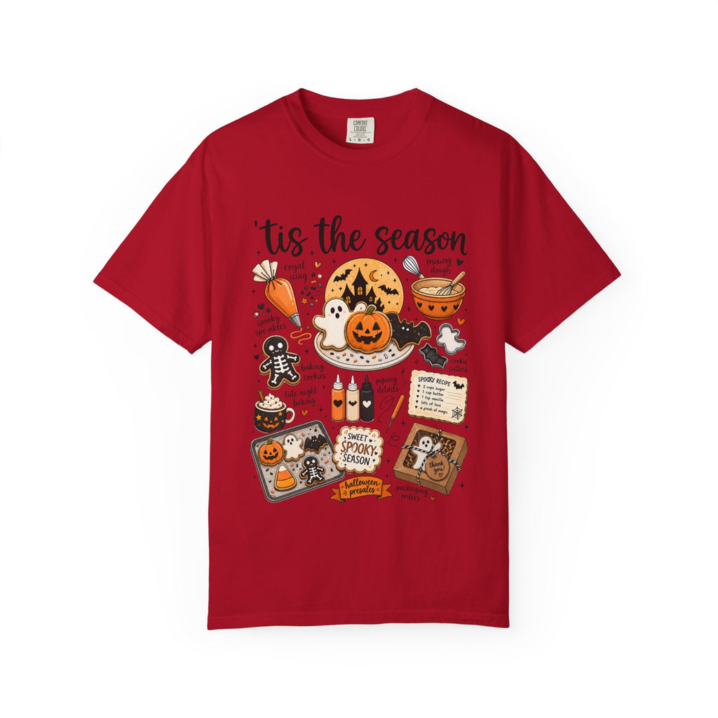 A red short-sleeve crewneck t-shirt featuring a colorful Halloween-themed graphic print on the front with the text 'tis the season' and illustrations of pumpkins, ghosts, treats, and a spiderweb.