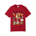 A red short-sleeve crewneck t-shirt featuring a colorful Halloween-themed graphic print on the front with the text 'tis the season' and illustrations of pumpkins, ghosts, treats, and a spiderweb.