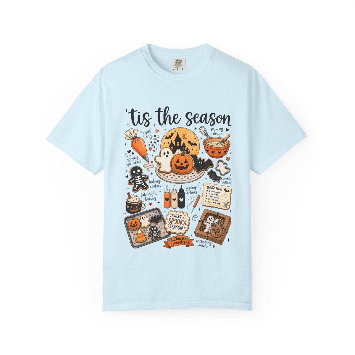 A light blue short-sleeve t-shirt with a detailed Halloween-themed graphic print on the front, featuring illustrations of a jack-o'-lantern, spider, gingerbread man, witch, and spooky decorations with the text 'tis the season'.
