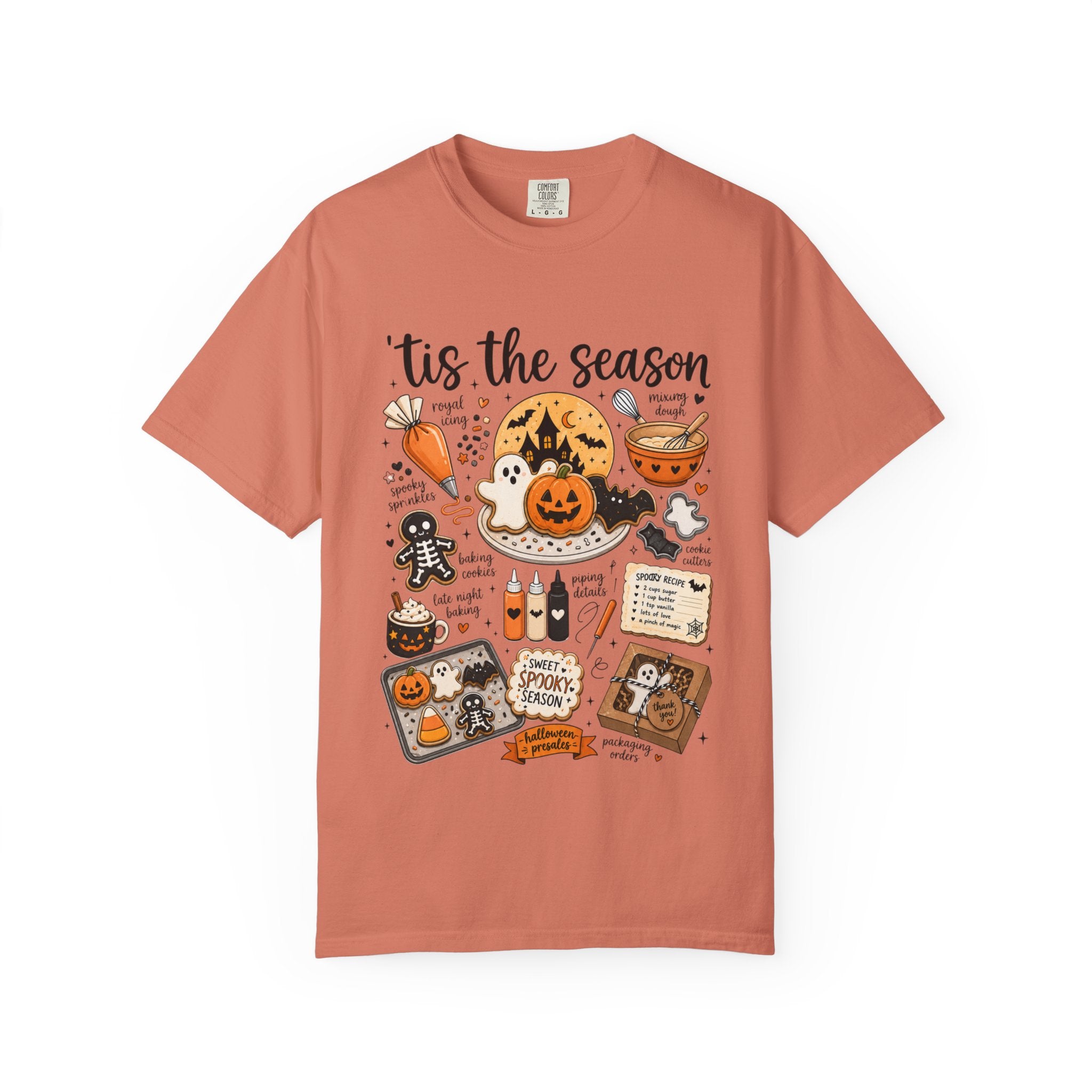 A coral pink crewneck t-shirt featuring a detailed, colorful Halloween-themed graphic print on the front with the text 'tis the season' and various spooky illustrations.