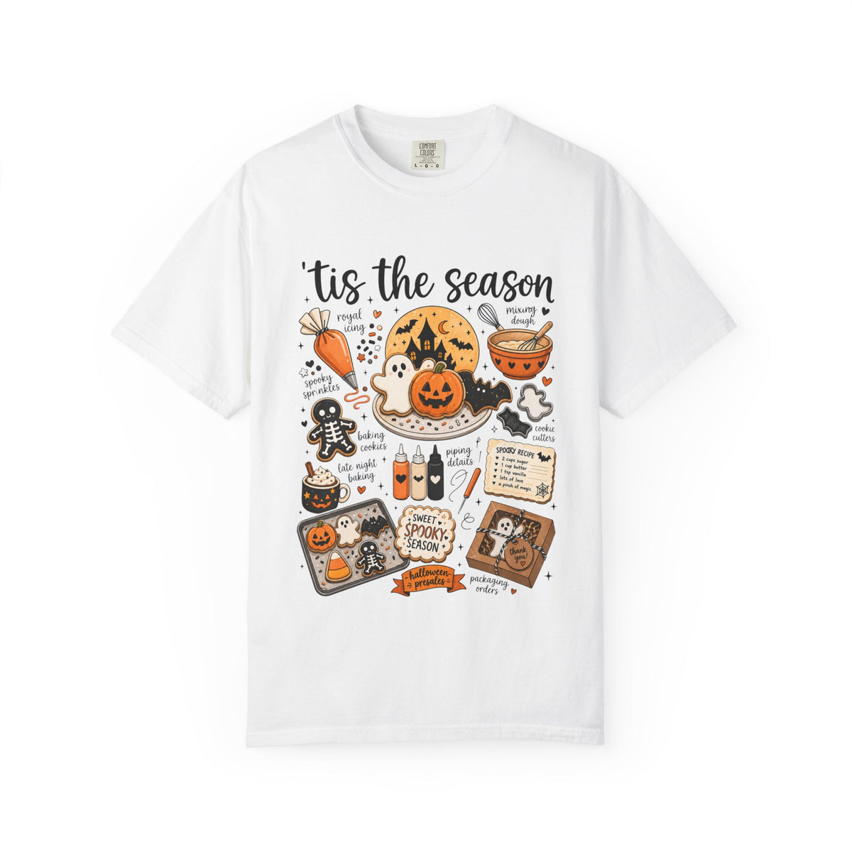 A white short-sleeve crewneck t-shirt featuring a colorful Halloween-themed graphic print on the front with the text 'tis the season' and illustrations of pumpkins, ghosts, a cauldron, and spooky treats.