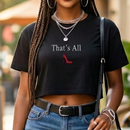Woman in black t-shirt, denim shorts, and red high heels standing on a sidewalk with outdoor cafe tables in the background.