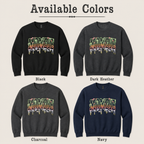 A color-options graphic titled 'Available Colors' showing four crewneck sweatshirts arranged in a 2x2 grid: Black, Dark Heather, Charcoal, and Navy. Each sweatshirt has a large dripping 'MOMBIE' graphic across the chest in multicolor tones.