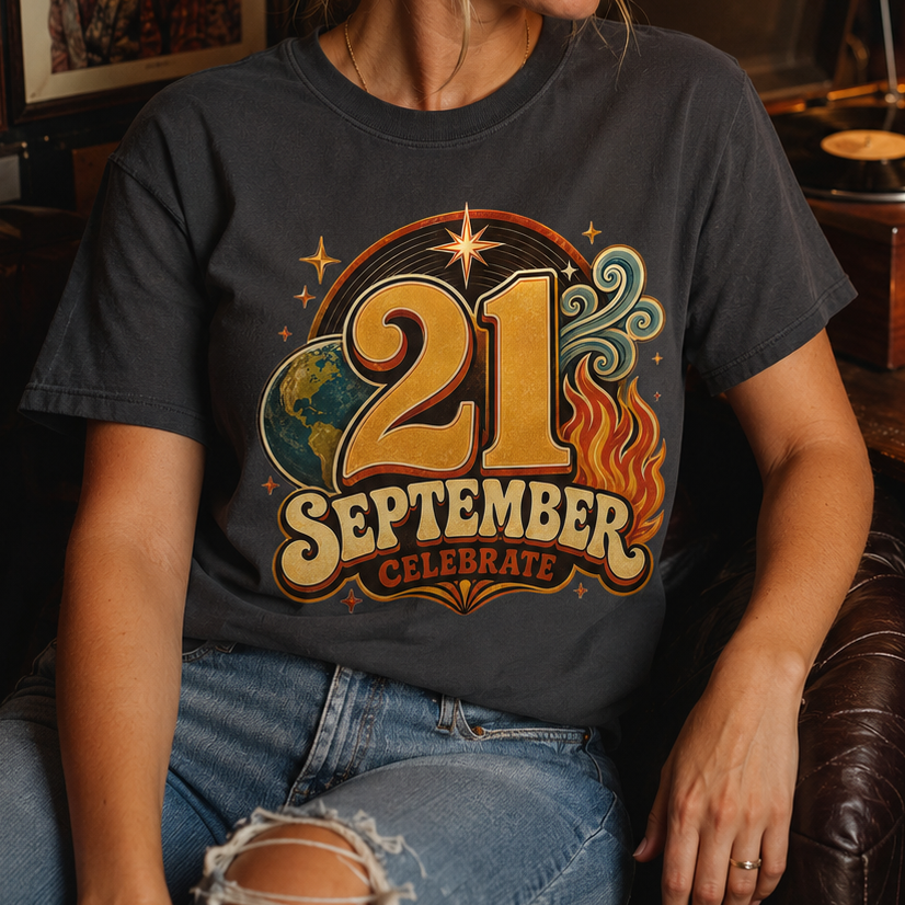 A woman wearing a dark charcoal gray graphic t-shirt that reads '21 SEPTEMBER CELEBRATE' with a retro gold, orange, and blue design, sitting in a cozy, dimly lit room with a record player and warm lamp in the background.