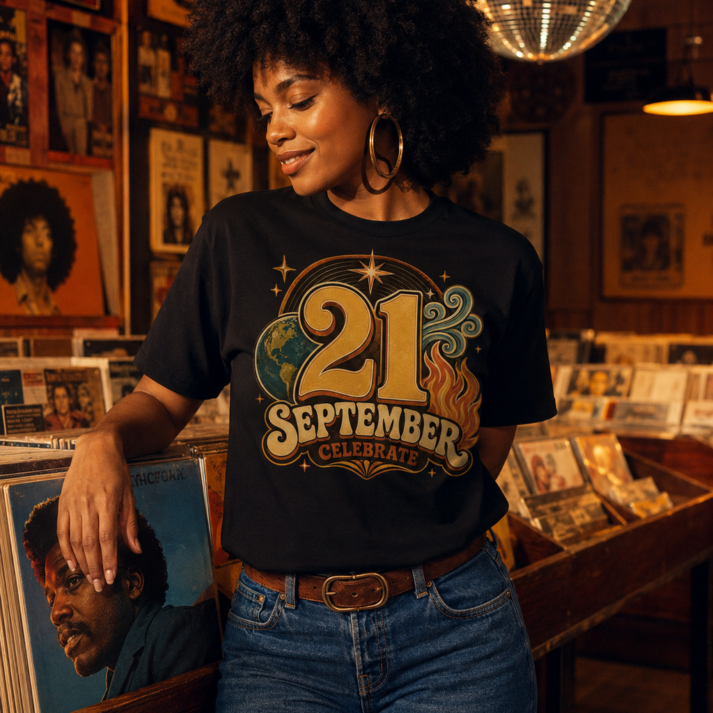 A woman with an afro hairstyle stands in a record store wearing a black graphic t-shirt that reads '21 SEPTEMBER CELEBRATE' in a retro gold and green design, paired with blue jeans.