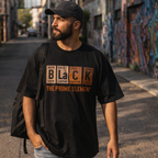 Man wearing a black t-shirt with text, standing in an alley with graffiti.