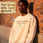 Man wearing a beige sweatshirt leaning against a brick wall with text above him.