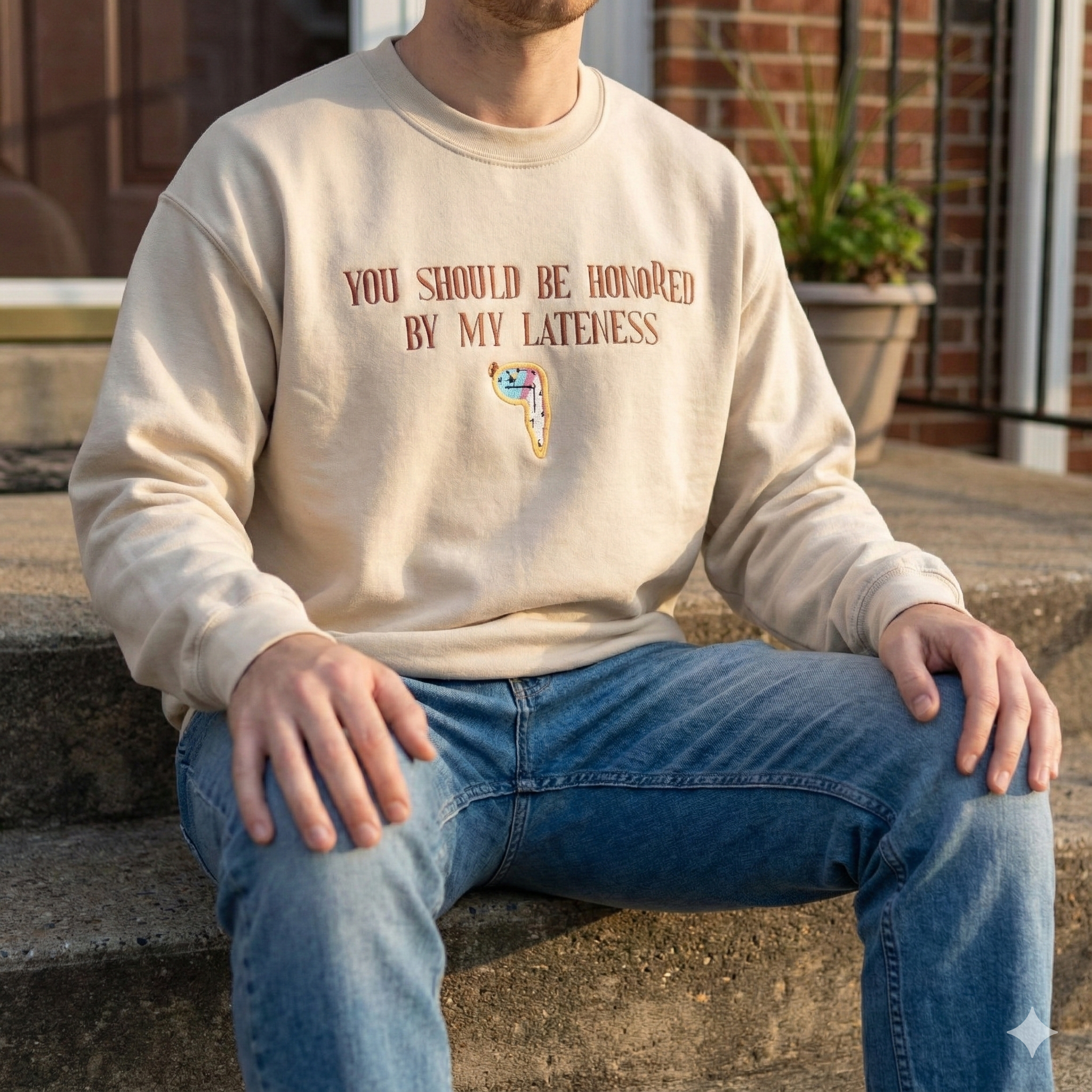 Person wearing a beige sweatshirt with text and a graphic, sitting on steps.