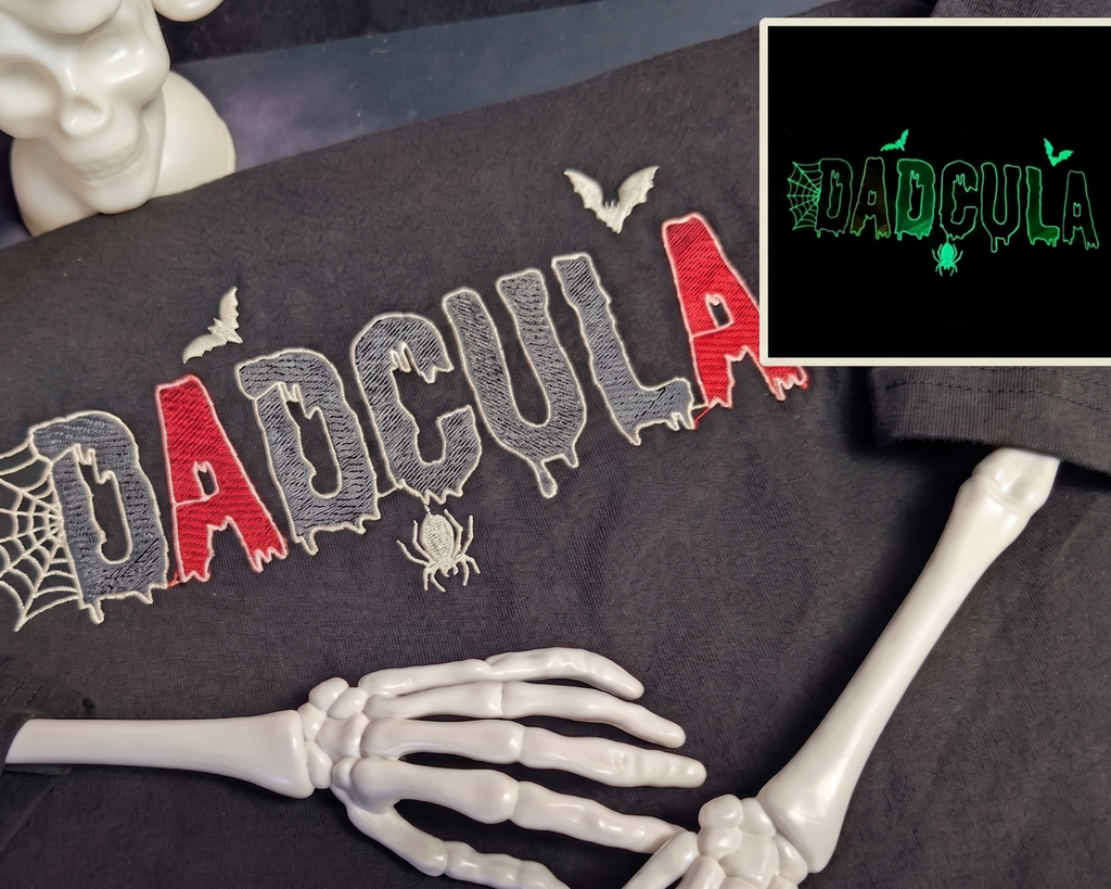 A black graphic sweatshirt featuring the word 'DADCU LA' in a dripping red and gray font with spiderweb and spider motifs. The sweatshirt is styled with skeleton hands and a white skull bust on a dark background.