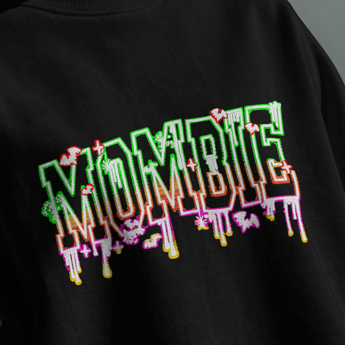 A person wearing a black crewneck sweatshirt with a colorful graphic text print reading 'MOMBIE' in dripping neon-style letters over a dark gray background.