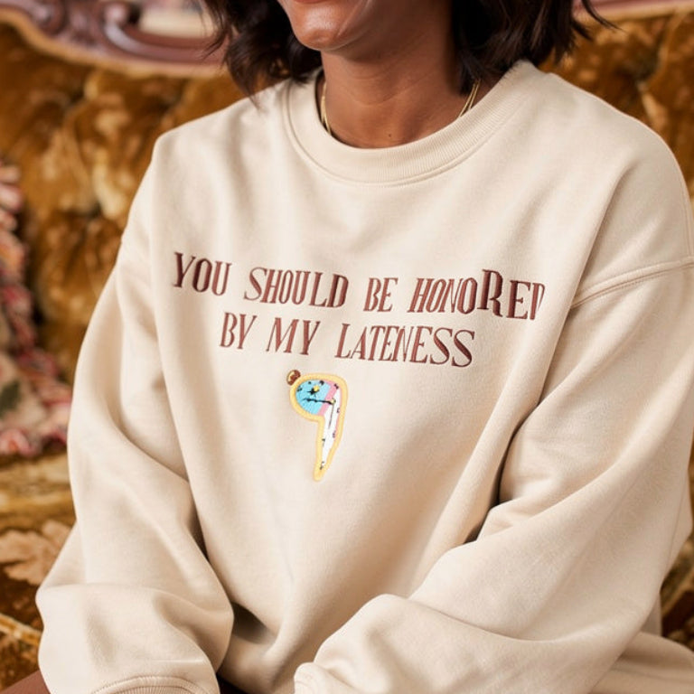 Woman wearing a cream sweatshirt with text and graphics, sitting on a patterned couch.
